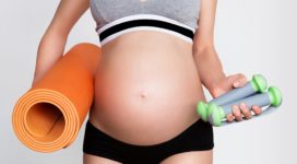 Young pregnant woman with beautiful healthy body holding dumbbells and mat